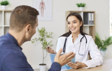 Ofiste oturan dost canlısı kadın doktor ya da kardiyolog hasta şikayetlerini dinliyor. Gülümseyen doktor ve erkek hasta klinikteki sağlık muayenesi sırasında tedaviyi tartışıyorlar.