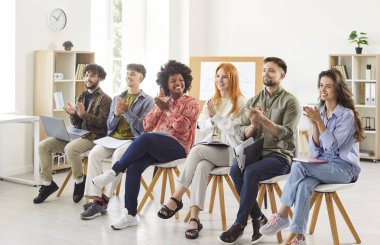 Sıraya dizilmiş sandalyelerde oturan mutlu gençlerden oluşan çok ırklı bir grup, iş toplantısından veya eğitimden sonra konuşmacıyı alkışlıyorlar. Müteşekkir şirket çalışanlarından oluşan farklı bir ekip meslektaşlarına ya da koçlarına el çırpıyor..