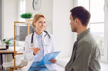 Modern klinikteki danışmanlık sırasında dost canlısı bir tıp çalışanı hastayla konuşur. Steteskoplu kadın doktor elinde kalem, not tahtası ve hasta ile konuşurken tıbbi kayıtlara geçiyor..