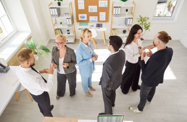 Modern ofiste toplanan bir grup profesyonel küçük gruplar halinde canlı tartışmalar yapıyorlar. Erkek ve kadın meslektaşlar toplantı sırasında fikir alışverişinde bulunup fikir alışverişinde bulunuyorlar..