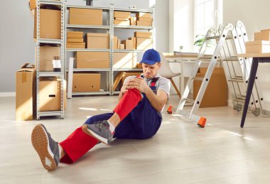 Sakatlık sonrası depoda çalışan erkek bir depo görevlisi yerde oturuyor. Çalışan adam, iş yerinde düştükten sonra bacağında ağrı hissediyor. Sağlık sigortası ve kaza çalışma kavramı