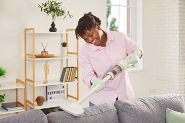 Üniformalı Afro-Amerikan hizmetçi kablosuz elektrik süpürgesiyle kanepeyi süpürüyor, yakın plan. Döşeme mobilyalarını temizleyen kadın. Konsept temizlik ekipmanları, kablosuz vakum