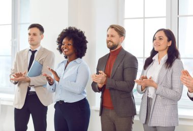 Bir grup mutlu iş adamı toplantı odasında sıra sıra beklerken hoparlörleri alkışlıyor. Başarılı iş arkadaşları ve şirket çalışanları iş eğitiminde veya konferansta bir meslektaşlarını alkışlıyorlar.
