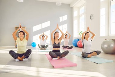 Yogi grubu, yoga dersi alan genç sporcular, beden eğitimi hocasıyla meditasyon yapan, egzersiz yapan, Lotus pozu veren, spor yapan, kulüpte, stüdyoda, namaste yapan arkadaşlar. 