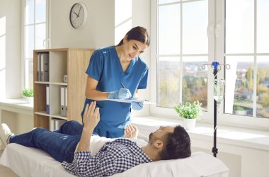 Genç bayan hemşire ya da doktor randevu ile rapor tutuyor ve klinikte kanepede yatan erkek hastasına danışmanlık yapıyor ve serum ve vitamin tedavisi görüyor..