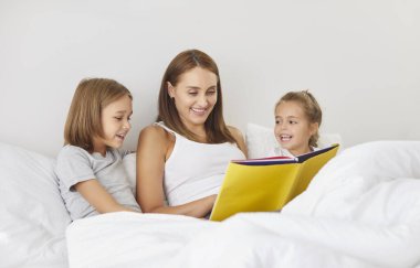 Yatağa yatmadan önce küçük şirin çocuklarına kitap okuyan mutlu bir annenin portresi. Aile eğlencesi ve uyku zamanı konsepti.
