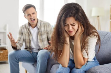 Kocası ona bağırırken çaresiz bir şekilde kulaklarını tıkayan sinirli kadını kapatın. Mutsuz bir çift evde kavga ediyor, kanepede oturuyor. Aile çatışması, boşanma, ayrılma.