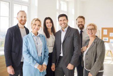 Modern ofiste duran, gülümseyen, çeşitli profesyonel iş adamları, kameralara bakan, genç ve yaşlı takım çalışanları grubu, ofiste insan kaynakları kurumsal portresi 