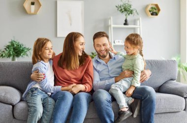 Gülümseyen dört çocuklu mutlu bir aile. İki kız ve erkek çocuk. Evde kanepede oturup hafta sonları dinleniyorlar. Çocuklu ebeveynlerin portresi. Aile zamanı ve eğlence konsepti.