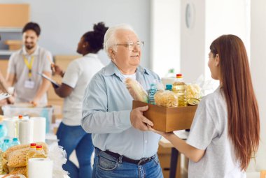 Gönüllü, sosyal yardım merkezinde yaşlı bir erkek emekliye bir kutu yiyecek veriyor. Yardım ve insani yardım örgütü, yaşlılara ve ihtiyacı olanlara yardım ve bağışta bulunuyor..