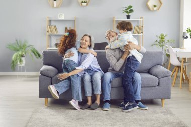 Büyükbaba ve çocuklar hafta sonu eğleniyorlar. Büyükannen ve büyükbaban çocukları görmekten mutlu. Büyükanne ve büyükbaba gri koltukta oturup torunlarına sarılıyorlar. İnsanlar, aile, aşk kavramları