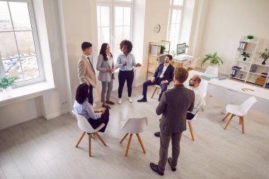 Resmi giysiler içinde kendine güvenen iş adamları toplantı odasında bir grup şirket çalışanı ile birlikte modern ofis konferansında şirket büyümesini tartışıyorlar..