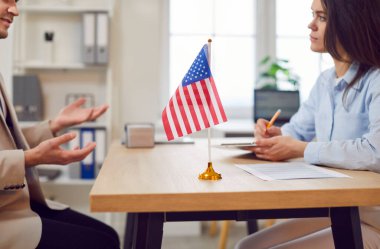 ABD kamu hizmetleri veya büyükelçiliğinde çalışan genç bir adam, iş yerinde elinde göçmenlik başvurusu bulunan Amerikan bayrağıyla kadın konsolosluk vizesi ile görüşme yapıyor..