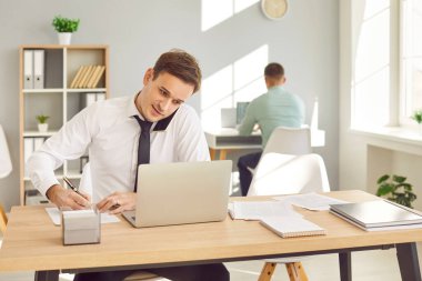 Ofiste dizüstü bilgisayarı olan bir iş adamı, bir müşteriyle telefon görüşmesi yapıyor. Profesyonel iletişim ve çoklu görev, iş adamı ve müşteri ya da müşteri sohbeti.