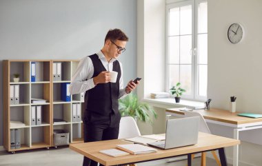 İş yerinin yanında bir fincan çay ya da kahveyle duran takım elbiseli, kendine güvenen genç bir işadamının portresi.