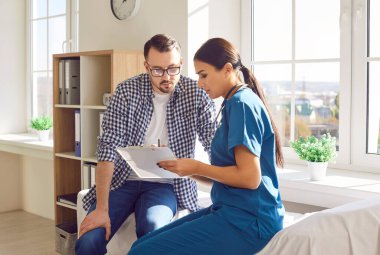 Tıp doktorluğundaki genç bir hastanın portresi klinikteki muayene sırasında elinde randevu ve danışmanlık ile rapor tutan dost canlısı bir kadın hemşireyi dinliyor..