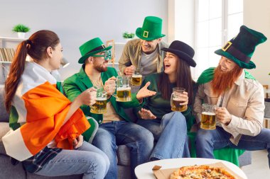 Aziz Patrick Günü etkinliği, arkadaş ev partisi, ulusal İrlanda kültürünün kutlaması, pizza, bira. Bir grup mutlu komik giyimli İrlandalı aptal yeşil şapka, sakal, İrlanda bayrağı, şenlik