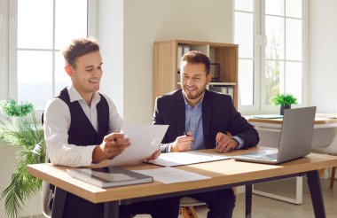 İki genç kendine güvenen iş adamı ve şirket çalışanı ofiste dizüstü bilgisayarla çalışıyor ve iş yerindeki mali belgelere bakıyor iş projelerini tartışıyorlar..