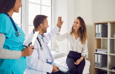 Muayeneden sonra klinikteki koltukta oturan mutlu kadın hastaya gülümseyen bir beşlik çakan hemşire ile genç bir doktor. Sağlık ve Tıp Konsepti.