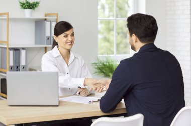 Ofis masasında oturan iki kişi iş anlaşması yapıyor ve el sıkışıyorlar. Sözleşme, ortaklık ya da iş sözleşmesi imzaladıktan sonra erkek müşteriyle tokalaşan gülümseyen kadın.