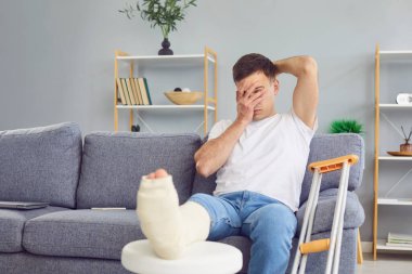 Kötü acı çeken bir adam, kırık bacağı ya da ayak yarası olan, koltuk değnekleriyle oturan, bacağı bandajlı hasta, rehabilitasyondan çıkmış, ayağı ağrıyan, yürüyemeyen, ciddi kırıklar olan.