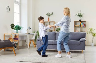 Genç, mutlu, beyaz bir anne evdeki oturma odasında çocuğuyla dans edip eğleniyor. Kadın ebeveyn oğluyla vakit geçirmekten zevk alıyor. Aile eğlencesi ve anneler günü konsepti.