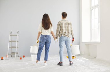 Boya kovaları olan bir çift duvarlara bakıyor, arkadan bakıyorlar. Tadilat yapılan bir odada el ele tutuşan genç adamlar. Yeni başlangıçlar, çift boyaları, ev tadilatı