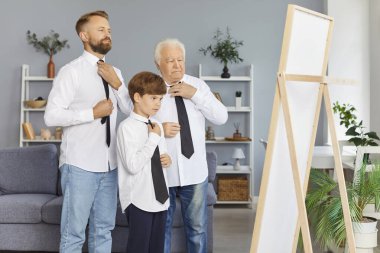 Aynaya kravat bağlayan üç nesillik bir aile. Büyükbaba, baba, oğul, çocuk torun. Aynı resmi kıyafeti giyip aile benzerliği gösteriyorlar.