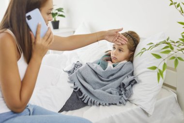 Endişeli genç bir anne, çocuk doktoru aile doktoruna evde soğuk algınlığı ya da gripten muzdarip hasta bir çocuğun sıcaklığını kontrol etmek için arıyor. Sağlık ve tıbbi danışma kavramı.