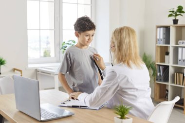 Kadın doktor çocuk doktoru steteskop kullanarak hasta bir çocuğun akciğerlerini dinliyor hastaneye yaptığı bir ziyarette. Sağlık uzmanları çocuğun solunum sağlığını sağlarlar.