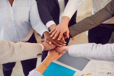 Meslektaşlardan oluşan bir ekip ellerini birleştirerek birlik ve isteklilik gösteriyor. İnsanlar ellerini birbirinin üstüne koyup takım ruhunu, motivasyonunu ve işbirliğini temsil ediyor..