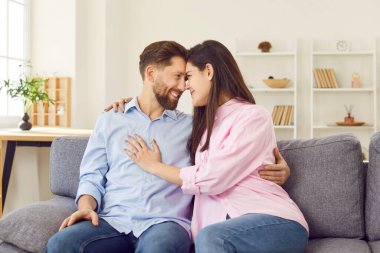 Aşk çifti kanepede oturmuş, sıkıca sarılıyor, gülümsüyor ve neşe saçıyor. Aşk çifti kucaklaşması, derin bir aşkı simgeler. Evde sıcaklık ve şefkat yaratır. Sevgili karı koca ve koca.