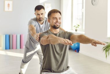 Erkek bakıcı ya da sağlık görevlisi rehabilitasyon merkezinde spor egzersizleri yapan genç bir hastaya yardım ediyor. Doktor fizyoterapist rehabilitasyondaki adama yardım ediyor. Fizyoterapi ve fizik tedavi konsepti.