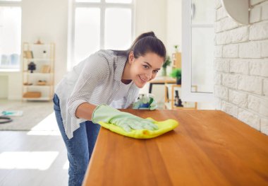 Plastik eldivenli, gülümseyen genç kadın mutfak tezgahının yüzeyini temizliyor deterjanla temizliyor. Ev işleri ya da ev işleri, temizlik hizmeti konsepti.