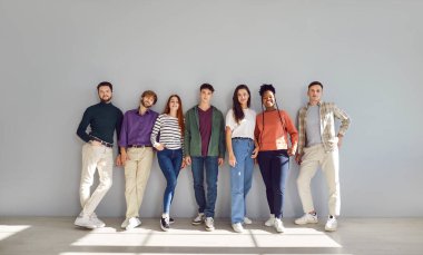 Yeni başlayanların genç takımı. Modern sektörde birlikte çalışan zeki, komik ve yaratıcı kadın ve erkeklerin portresi. Gülümseyen çok ırklı insanlar, ofiste gri duvarın önünde sıra sıra bekliyorlar.. 