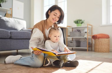 Sevgi dolu genç bir anne, bebek bakıcısı ve kitap okuyan küçük bir çocuk, evde birlikte oynadığımız komik bir hikaye sıcak zemin, oyun zamanı, yaratıcı annelik bakımı, okul öncesi aile etkileşimi
