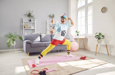 Evde esneme hareketleri yapan komik bir adam, cep telefonu kullanarak çevrimiçi sosyal medya için selfie çekiyor. Spor ve spor eğitimi sporun ve egzersizin eğlenceli yanlarını vurguluyor..