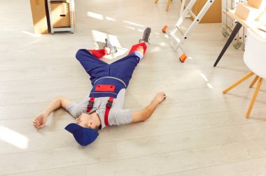 Yükleyici güvenlik prosedürlerine uymadığı için ciddi bir düşüşten sonra yerde baygın yatıyor. Depo zemininde yatan işçinin yüksek açılı görüntüsü. Güvenlik ekipmanları ve sigorta davaları kavramı.