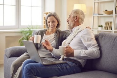 Kanepede oturup dizüstü bilgisayar başında film izleyen mutlu yaşlı çift. Birlikte dizüstü bilgisayarda film izleyip çay içerken yaşlı bir çift dizüstü bilgisayardan film seyrediyor.