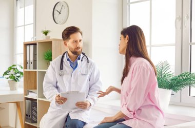 Muayene odasındaki klinikte genç bir kadın hastayla konuşan bir erkek doktorun portresi. Doktor muayenede bir kadına danışıyor. Tıp konsepti.