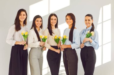 Uluslararası Kadınlar Günü 'nde çiçekli mutlu bayan iş ekibi. Sarı laleleri tutan ve gülümseyen güzel genç kadınların toplu portresi. Tatil kavramı