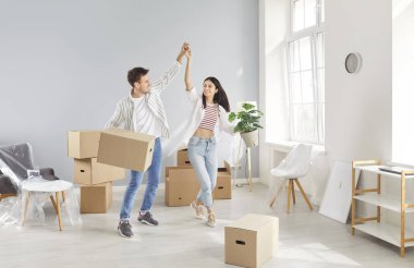 Heyecanlı ev sahipleri, kiracılar, yeni bir daireye taşınmaktan mutlu, kutuları taşımaktan mutlu, evli genç çift ilk eve taşınmaktan zevk alıyor, erkek ve kadın çift taşınmaktan mutlu, neşe içinde dans ediyorlar.