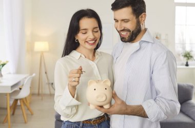 Mutlu, genç, gülümseyen bir çift kumbarayı tutuyor ve paraları evde yan yana koyuyorlar. Neşeli adam ve kadın para planlama bütçesinden tasarruf ediyorlar. Yatırımlar ve finansal özgürlük kavramı.