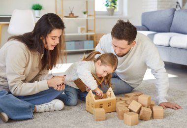 Genç mutlu anne ve baba evdeki oturma odasında küçük tatlı bir kızla eğitici tahta oyuncaklarla oynuyorlar. Ebeveynler kızlarıyla vakit geçiriyor. Aile eğlencesi ve insan konsepti.