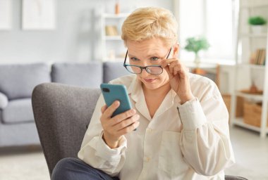 Üst düzey yaşlı bayan akıllı telefon ekranında uygulamalar kullanıyor, olgun bir kadın arkadaşlarıyla ya da çocuklarıyla mesajlaşma ya da sosyal ağda sohbet ediyor, internet mağazasında alışveriş yapıyor, internette gülümsüyor.