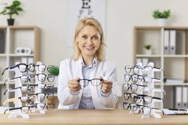 Kadın doktor göz doktoru görüş için gözlük tutuyor, yakın plan. Optikte, bir uzman gözlük seçmeye yardımcı olur. Konsept sağlık ve ilaç, büyüteç, göz bakımı, optik