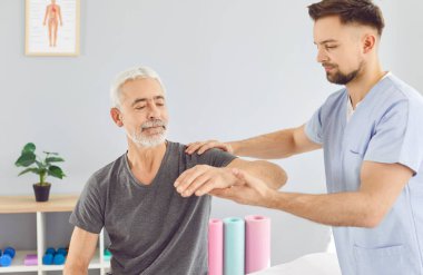 Fizyoterapist, yaşlı beyaz saçlı emekli erkek hastaya felç geçirdikten sonra dirsek hareketliliği kazandırıyor. Fizyoterapi kliniği, fizyoterapi, yaşlı hastalar için tıbbi rehabilitasyon