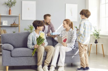 Anneler Günü 'nüz kutlu olsun, anneler ve küçük oğullar, tebrik, hediye kutusu, aşk sembolü ve çiçekli el yapımı kart, evde tatil hediyesiyle heyecanlanan gülen koca.