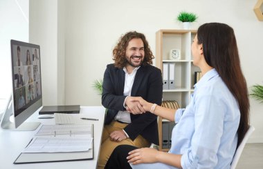 Tatmin olmuş iki meslektaş, başarılı bir anlaşmadan sonra iş temsilcileriyle çevrimiçi toplantı yaptı ve el sıkıştı. Bilgisayarın karşısında oturan gülümseyen insanlar ve başarı için birbirlerini tebrik eden insanlar..