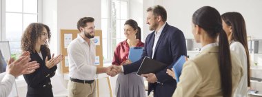 Mutlu erkek patron, iyi bir iş çıkardığı, el sıkıştığı, terfi ettiği, saygı duyduğu ve yeni takım üyesini tanıttığı için ofis çalışanlarını cesaretlendirdiği ve teşekkür ettiği için elini sıkar.